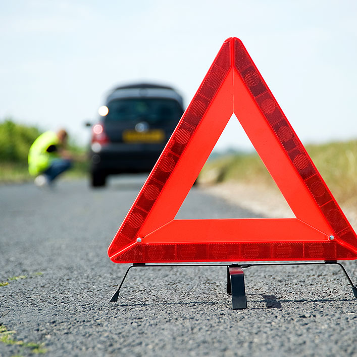 Una señal de advertencia de triángulo rojo al costado de la carretera que indica peligros potenciales más adelante.